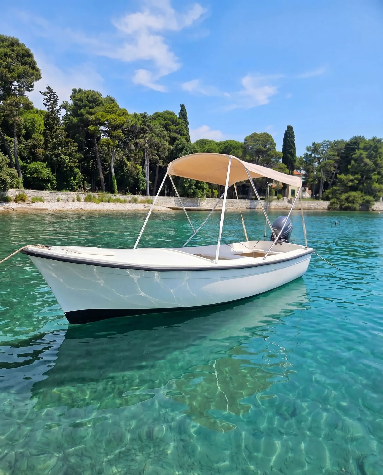 A traditional white Pasara, bimini sun-shade up, moored in the clear turquoise shallows off Rovinj.